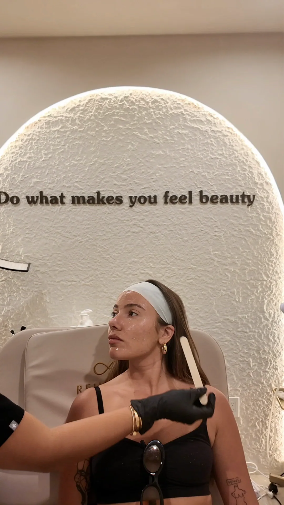 A practitioner smooths a treatment onto a client's cheek with a spatula under the arch reading Do what makes you feel beauty