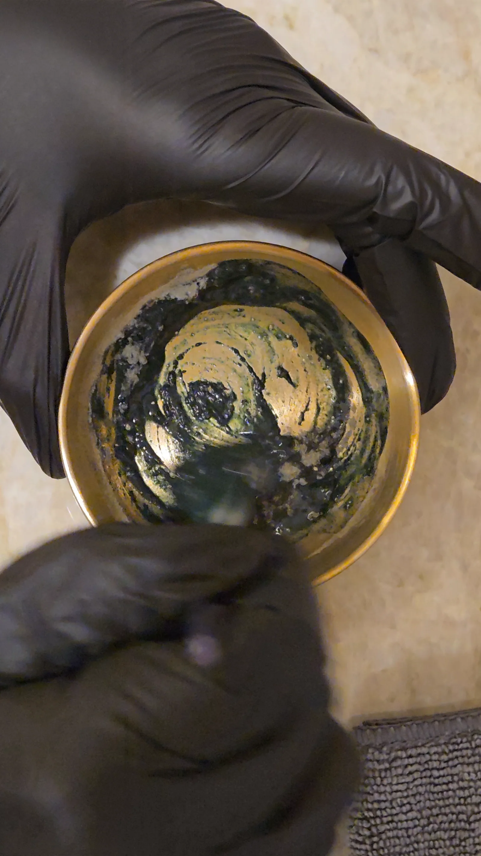 Gloved hands mix a green peel in a gold bowl