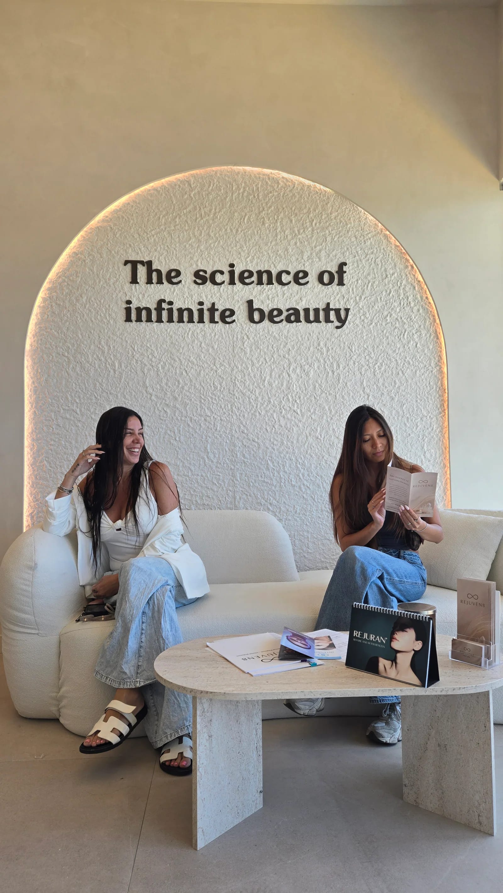 Two clients on the lobby sofa under the arch reading The science of infinite beauty