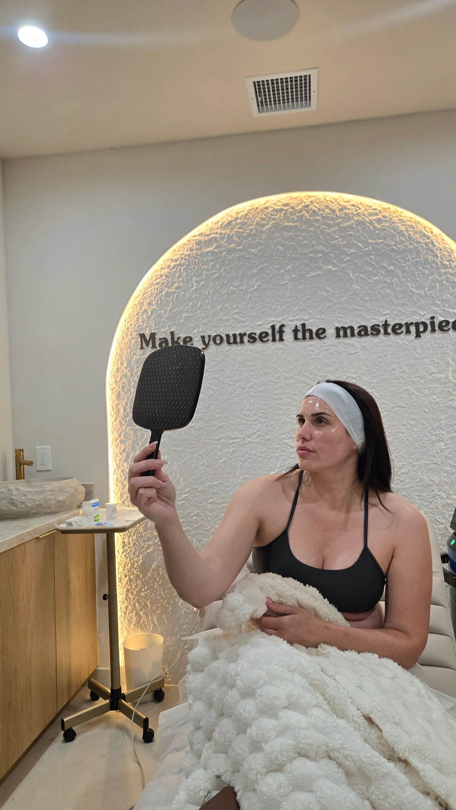 A client in a post-treatment face mask checking her skin in a hand mirror