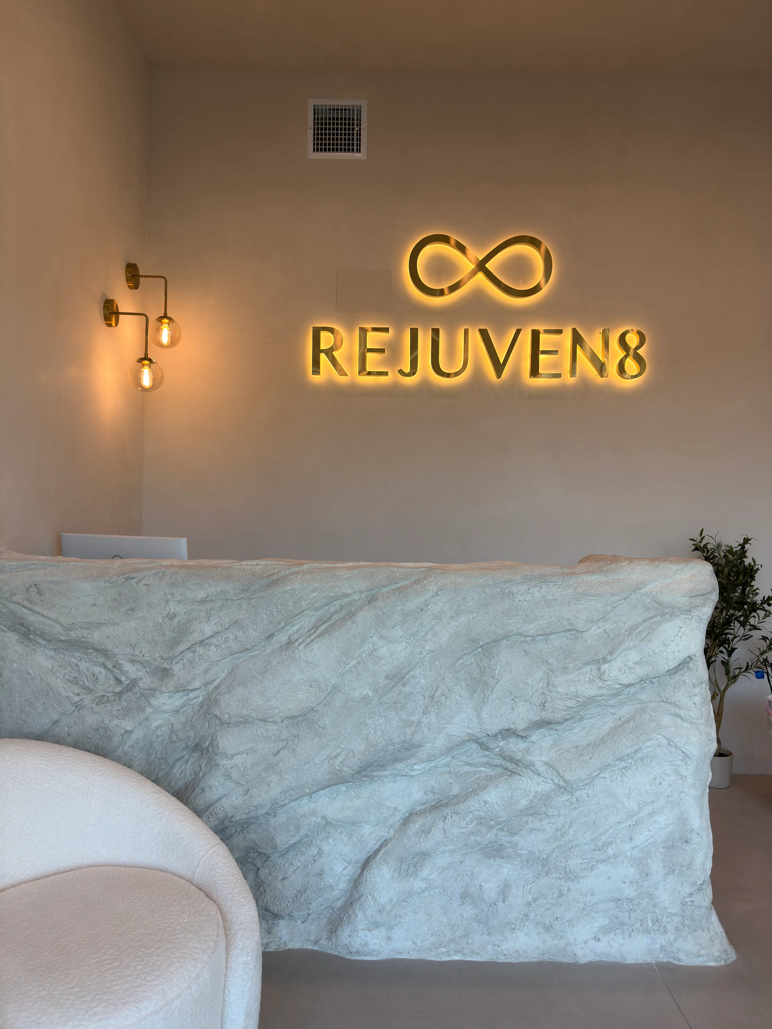 The rock reception desk under the lit gold Rejuven8 sign