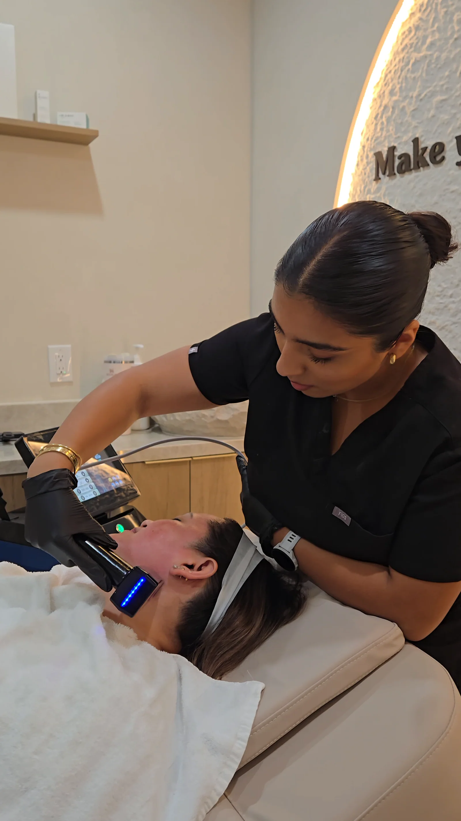 A practitioner in black scrubs works an RF microneedling handpiece along a client's jaw