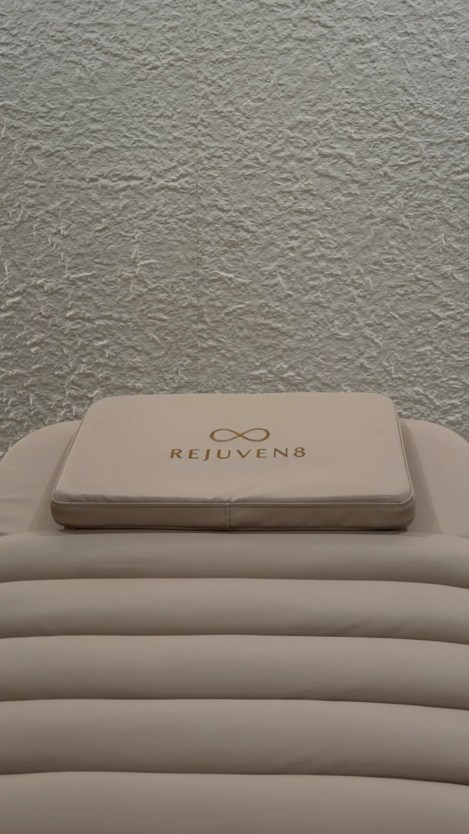 A Rejuven8 treatment bed and its logo pillow against the textured arch wall