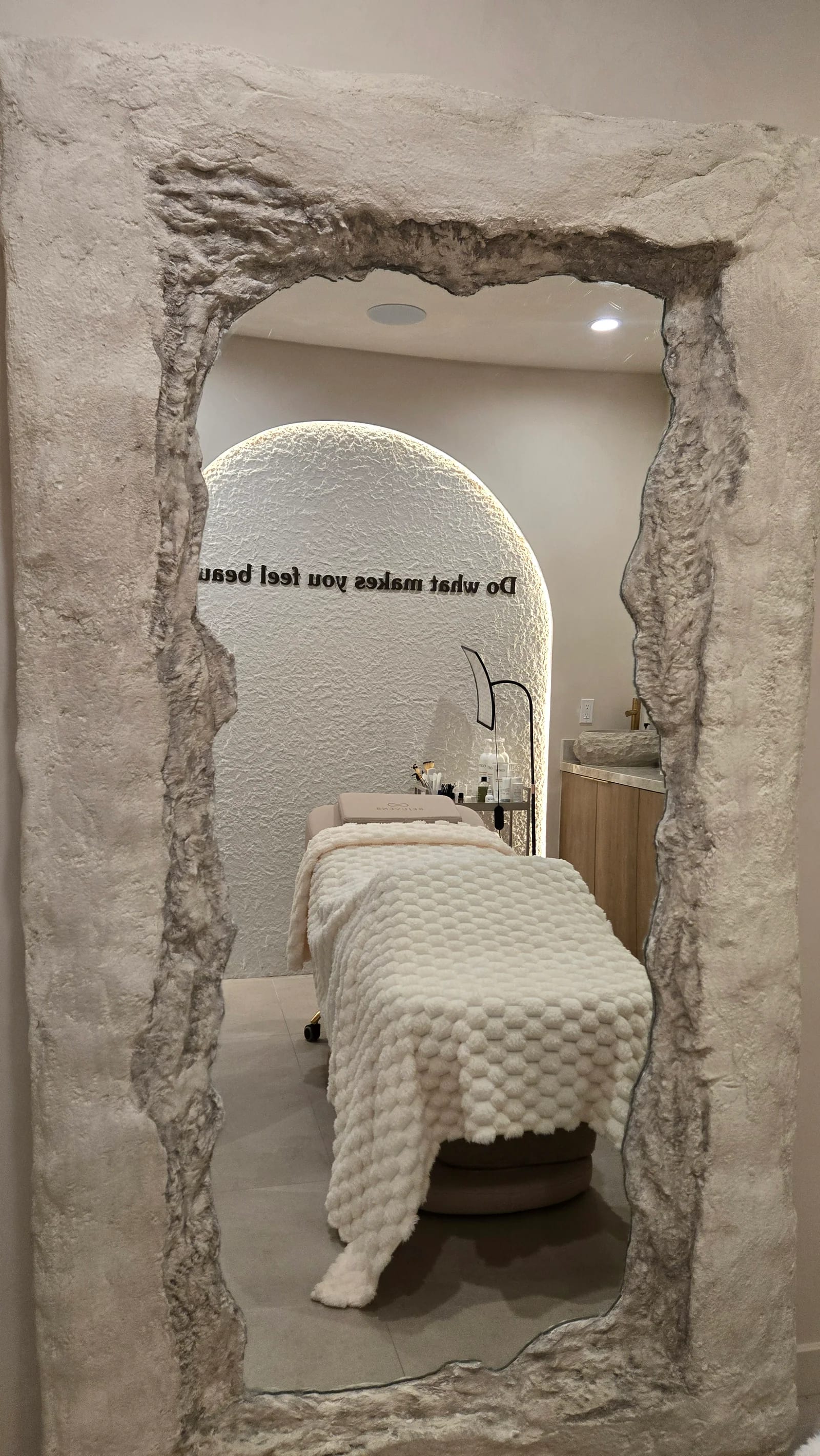 A made treatment bed reflected in the rock-framed mirror of a Rejuven8 treatment room