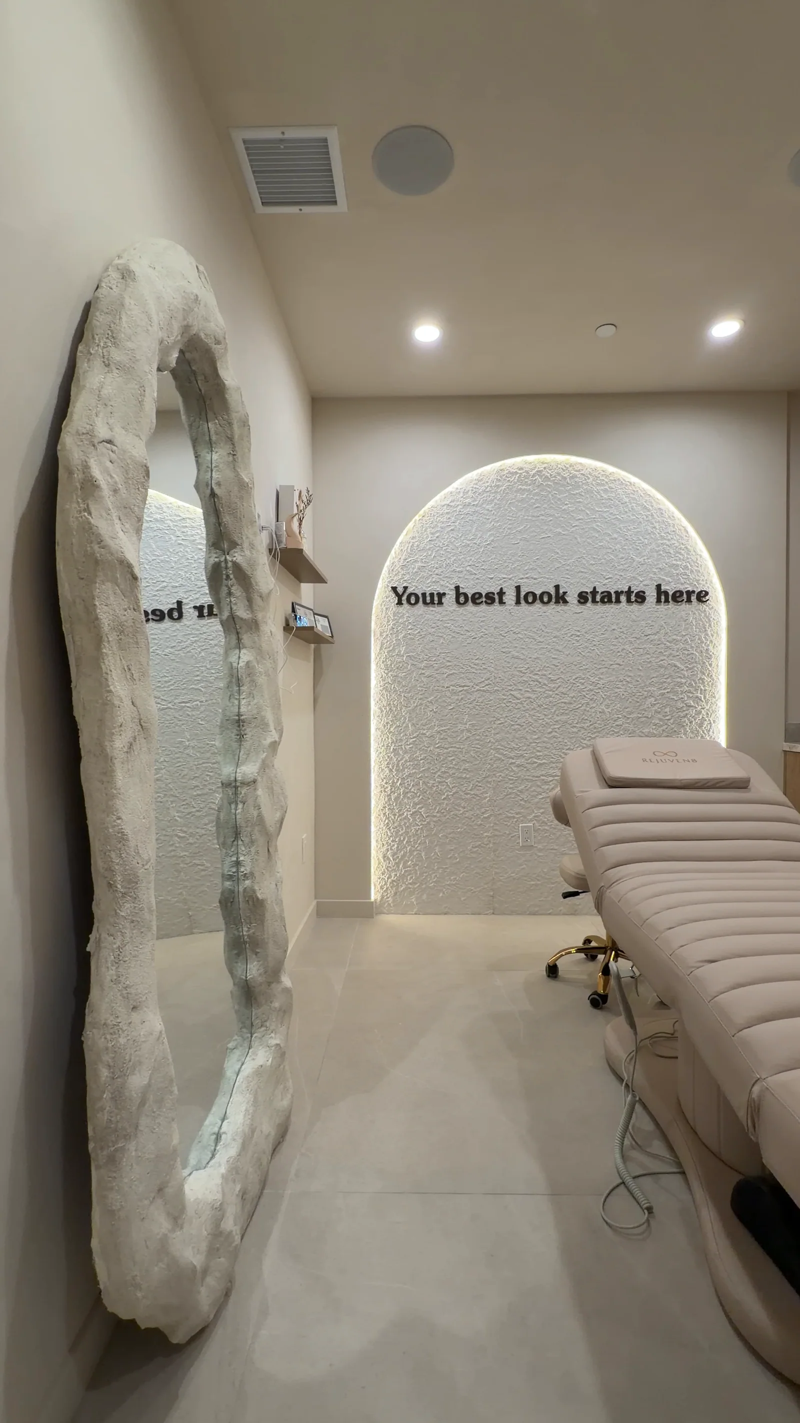 A treatment room seen past the rock-framed mirror, its lit arch reading Your best look starts here