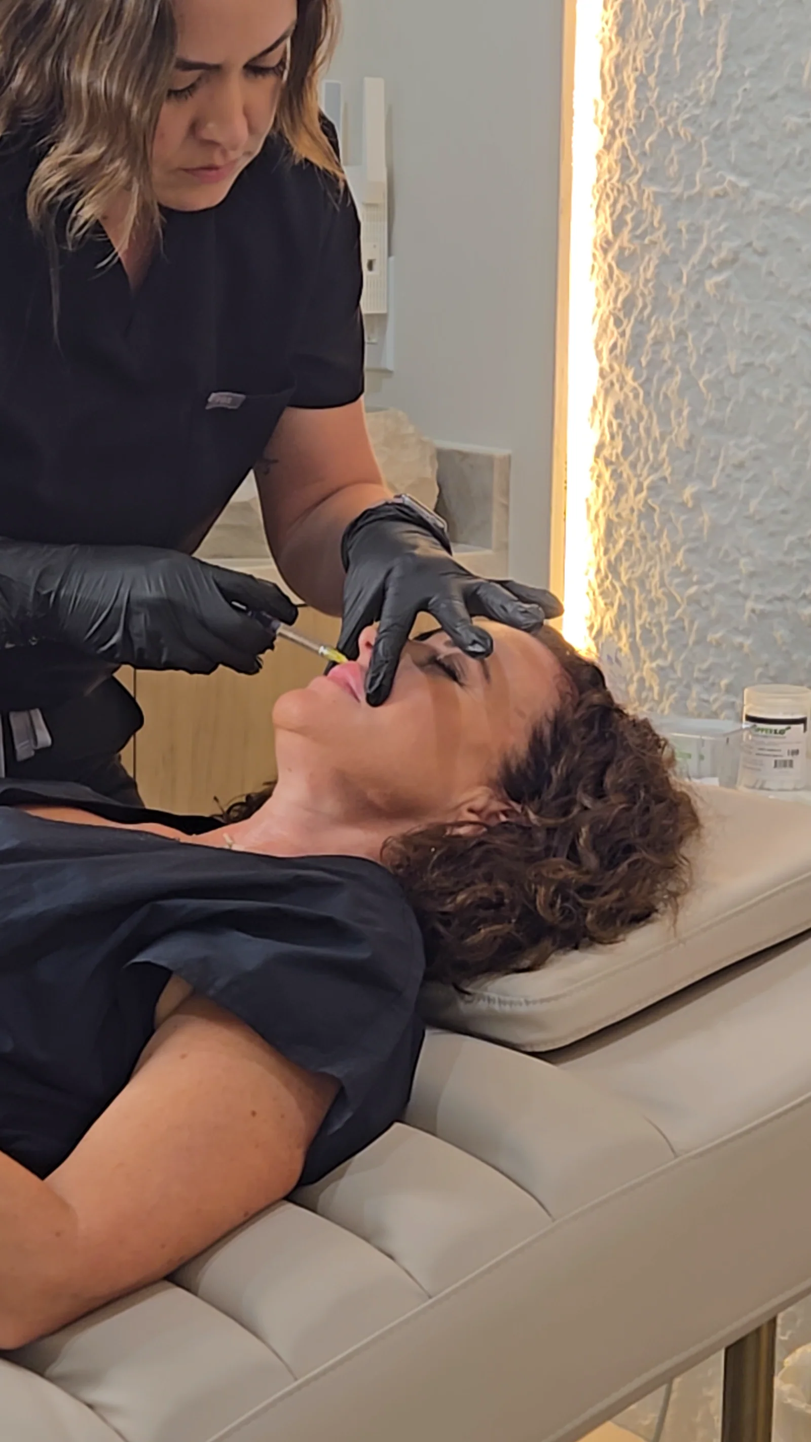 A practitioner treats the lip area of a client reclining on the treatment bed