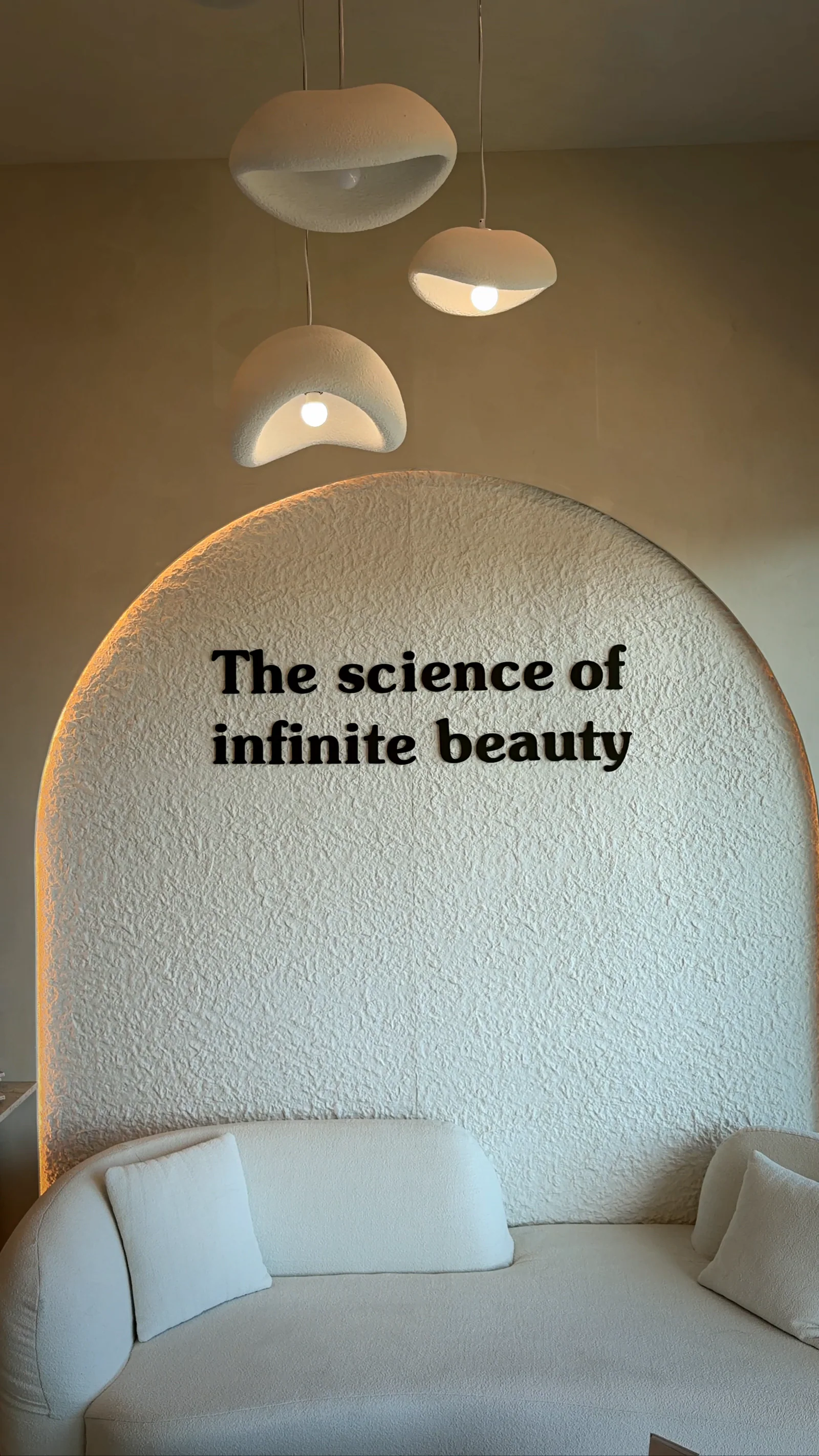 Pendant lamps above the lobby sofa and the lit arch reading The science of infinite beauty