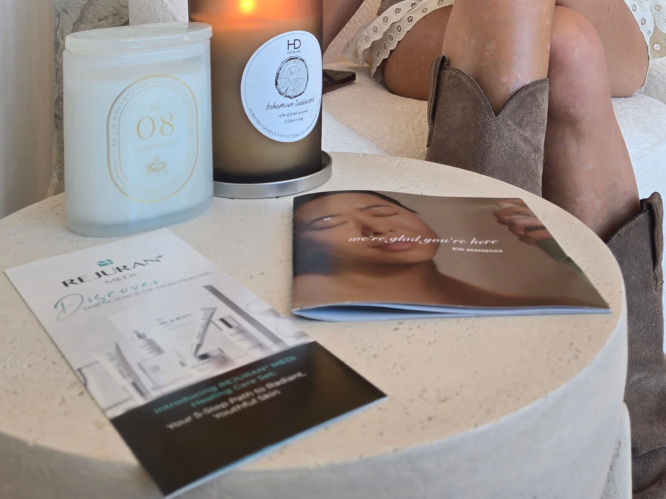A Rejuran brochure and two lit candles on the stone side table in the Rejuven8 lobby, a client seated beside it
