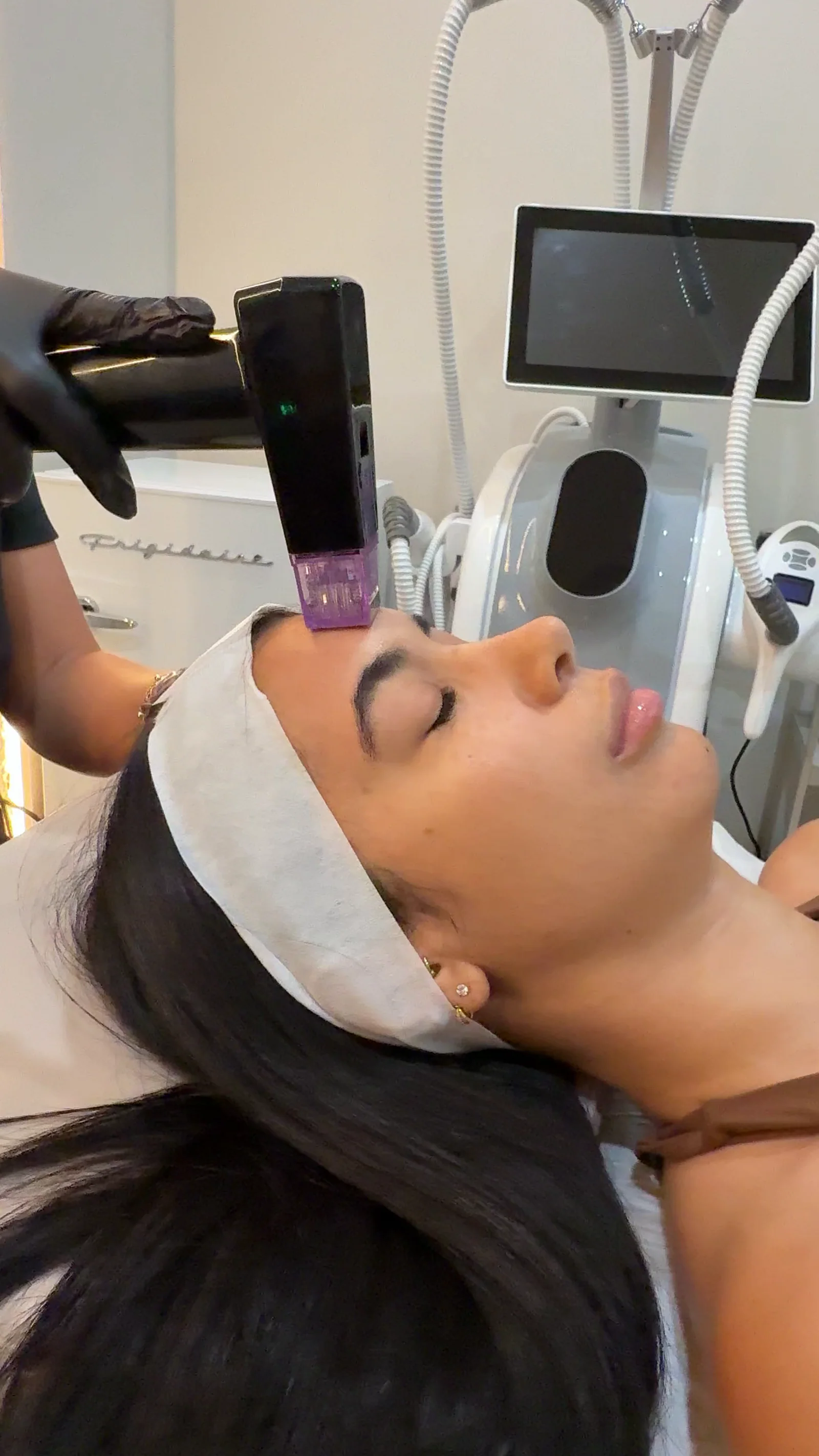 An RF microneedling handpiece with a purple tip placed on a client's forehead