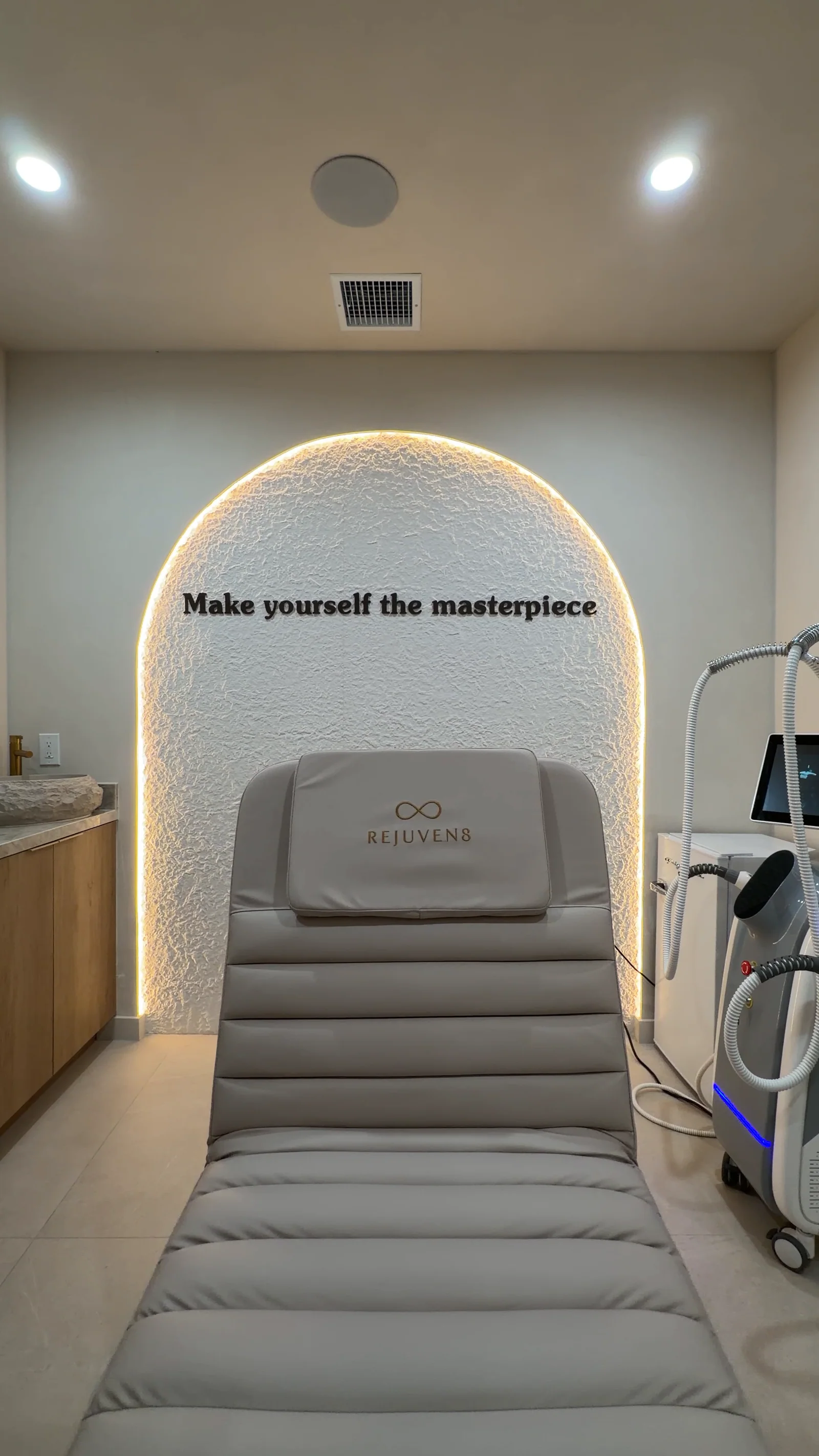 A Rejuven8 treatment chair under the lit arch reading Make yourself the masterpiece, the body contouring machine beside it